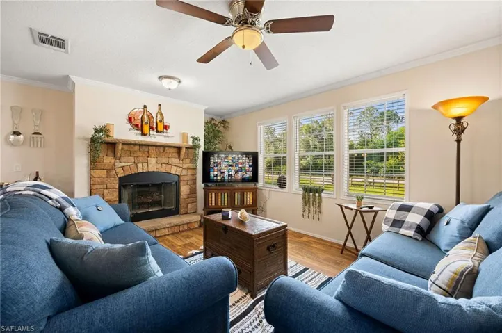 Living room featuring a fireplace, ornamental molding, hardwood / wood-style flooring, and ceiling fan