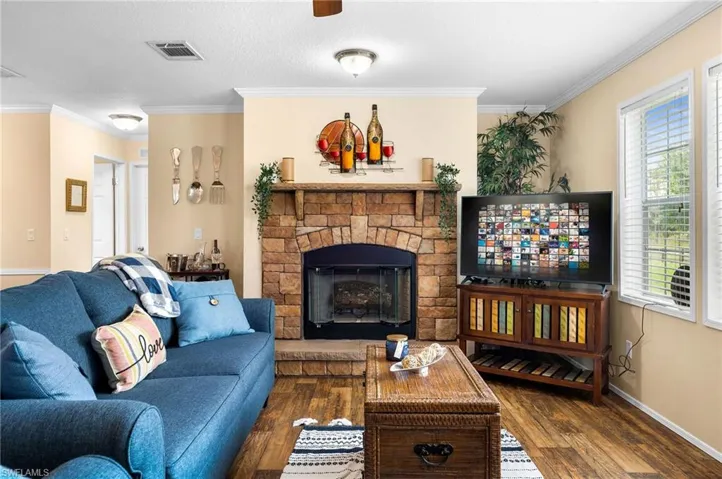Living room featuring ornamental molding, a wealth of natural light, a stone fireplace, and dark hardwood / wood-style floors