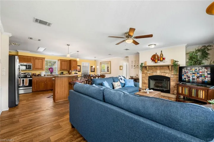 Living room with dark wood-type flooring, ceiling fan, a stone fireplace, and a healthy amount of sunlight