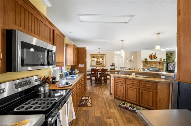 Kitchen featuring hanging light fixtures, a fireplace, appliances with stainless steel finishes, sink, and dark wood-type flooring