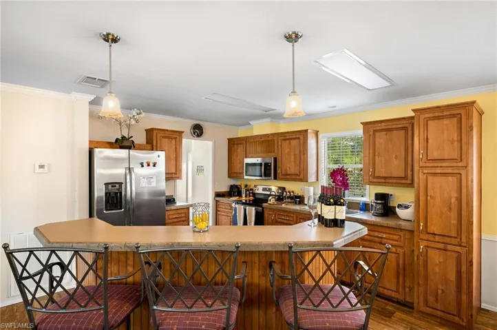 Kitchen featuring hanging light fixtures, crown molding, stainless steel appliances, and a large island