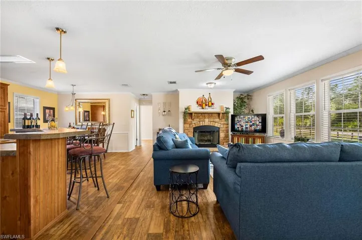 Living room featuring crown molding, dark wood-type flooring, ceiling fan with notable chandelier, and a fireplace