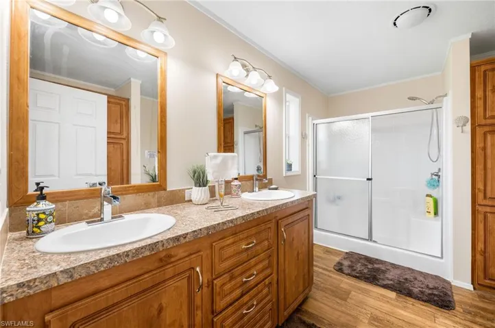 Bathroom with ornamental molding, vanity, hardwood / wood-style flooring, and a shower with shower door