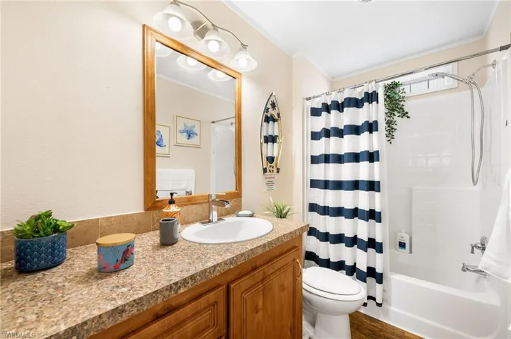 Full bathroom featuring crown molding, hardwood / wood-style floors, toilet, shower / tub combo with curtain, and vanity