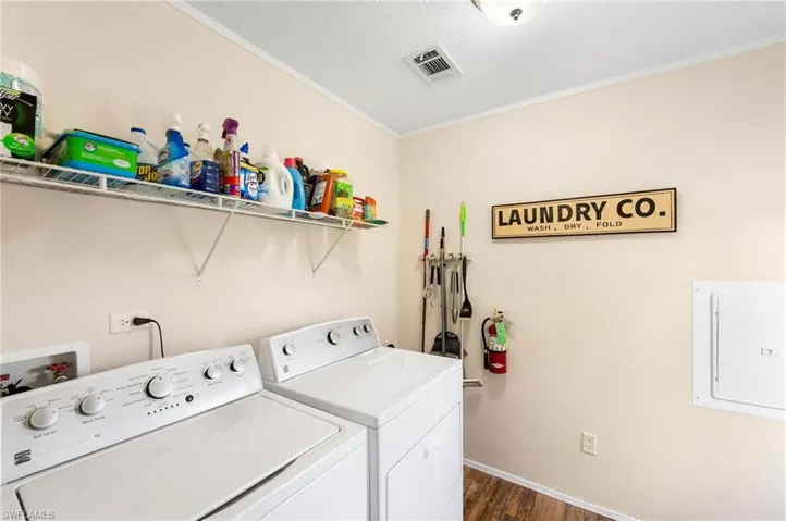 Clothes washing area featuring crown molding, washer and dryer, electric panel, and dark hardwood / wood-style floors