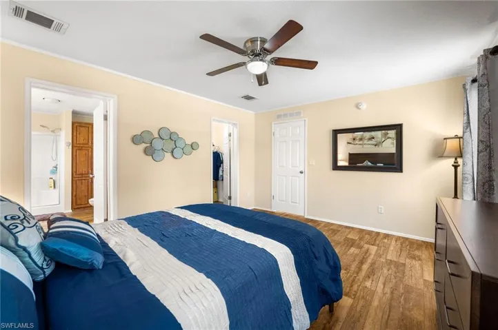 Bedroom with crown molding, connected bathroom, wood-type flooring, ceiling fan, and a closet