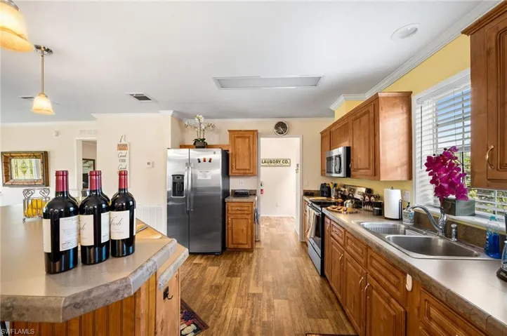 Kitchen with hardwood / wood-style flooring, crown molding, decorative light fixtures, appliances with stainless steel finishes, and sink