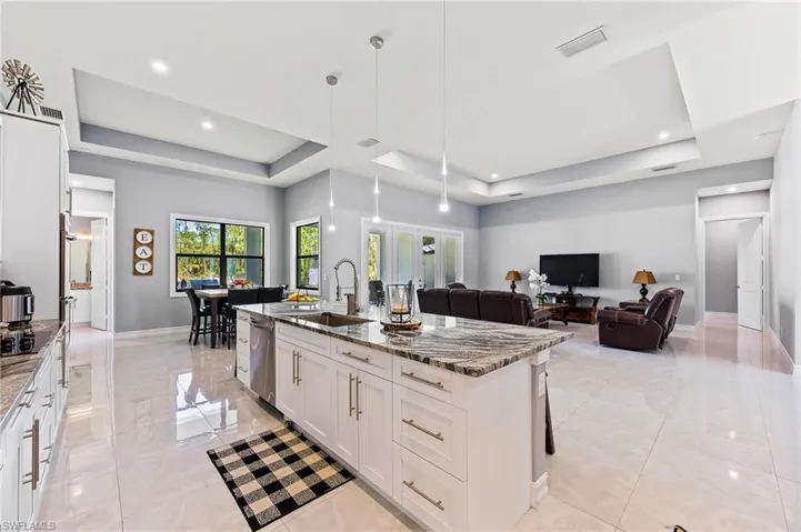 Kitchen featuring a raised ceiling, light tile flooring, a kitchen island with sink, and sink