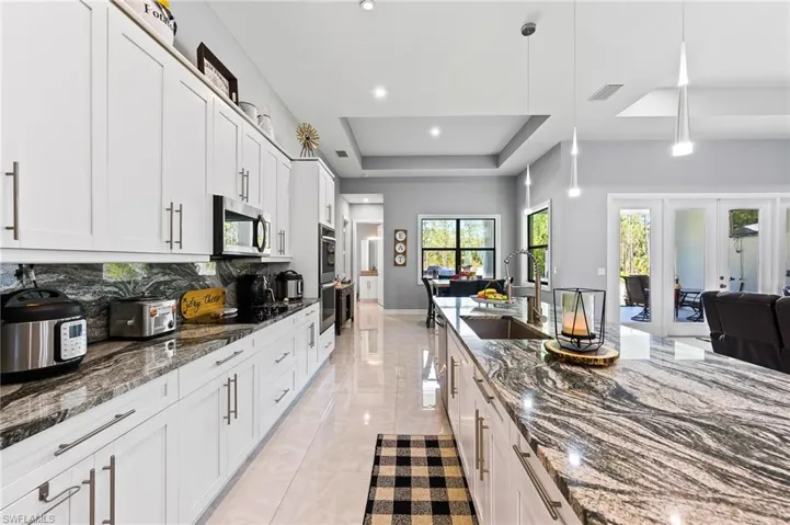 Kitchen with stainless steel appliances, dark stone counters, sink, tasteful backsplash, and a raised ceiling