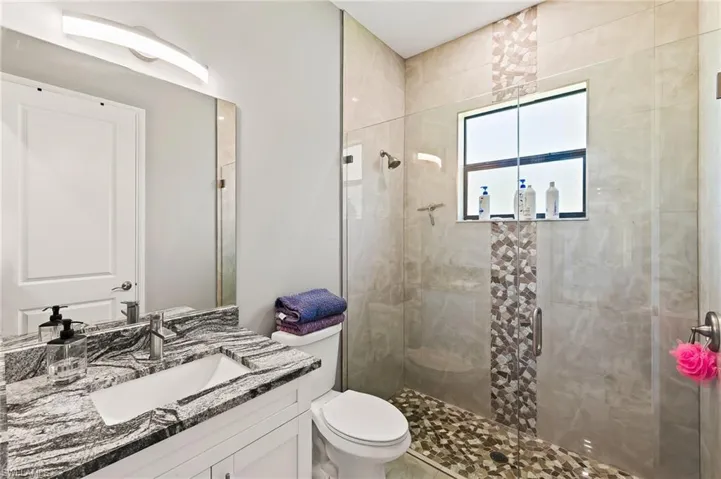 Bathroom featuring a shower with door, toilet, and large vanity