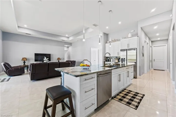 Kitchen with white cabinetry, hanging light fixtures, an island with sink, appliances with stainless steel finishes, and a raised ceiling