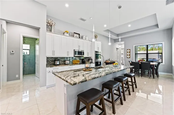 Kitchen featuring appliances with stainless steel finishes, white cabinetry, an island with sink, and pendant lighting