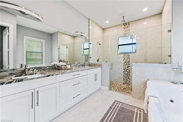 Bathroom featuring oversized vanity, double sink, tile walls, plus walk in shower, and tile floors