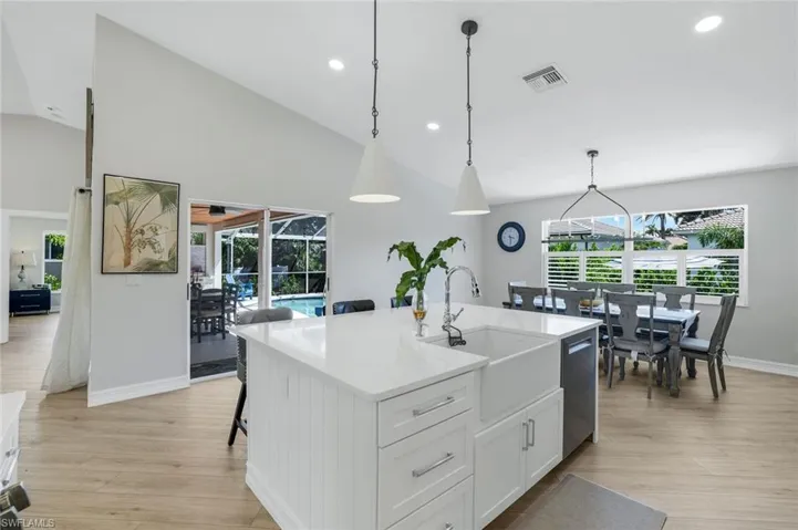 Kitchen with white cabinets, a breakfast bar, hanging light fixtures, a center island with sink, and light stone counters