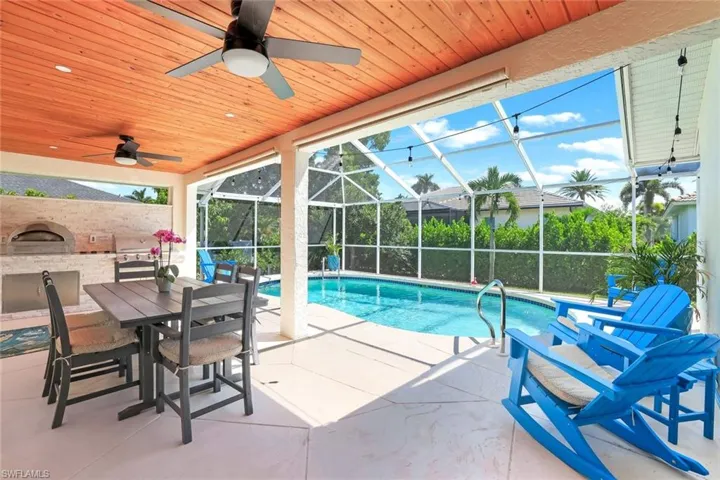 Swimming pool featuring a sunroom, a patio, a lanai, an outdoor kitchen, and outdoor dining space