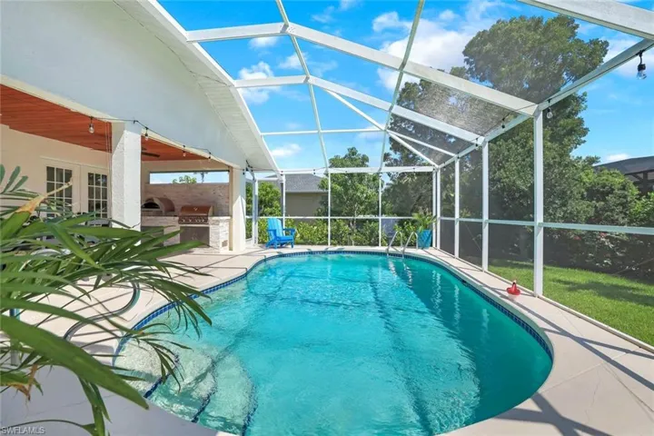 Outdoor pool with area for grilling, a patio area, glass enclosure, a sunroom, and a yard