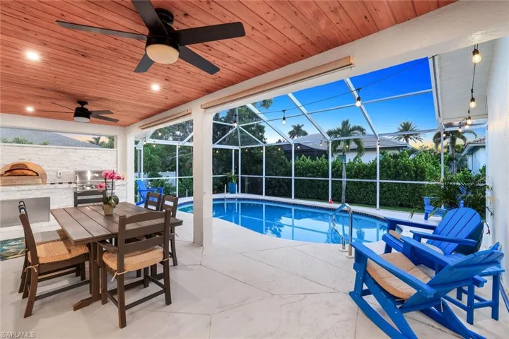 Outdoor pool with a sunroom, a patio, glass enclosure, exterior kitchen, and outdoor dining space