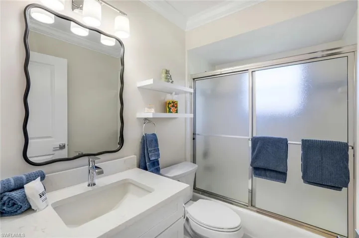 Full bath featuring vanity, crown molding, and bath / shower combo with glass door