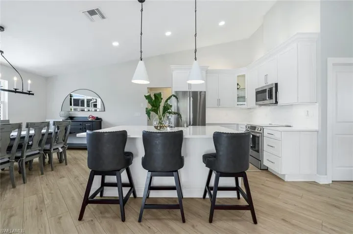 Kitchen featuring hanging light fixtures, glass insert cabinets, appliances with stainless steel finishes, white cabinetry, and a center island