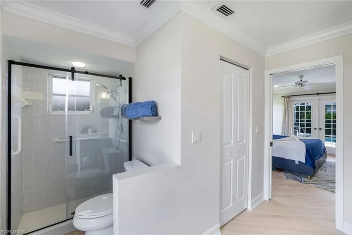 Ensuite bathroom featuring french doors, a shower stall, light wood finished floors, a closet, and crown molding