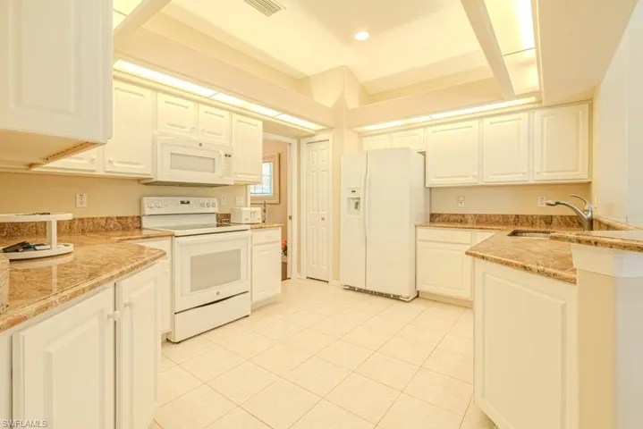 Kitchen featuring white cabinets, light stone counters, light tile flooring, sink, and white appliances