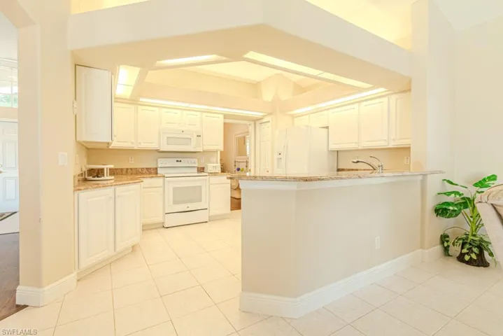 Kitchen with light stone counters, white cabinets, white appliances, and kitchen peninsula