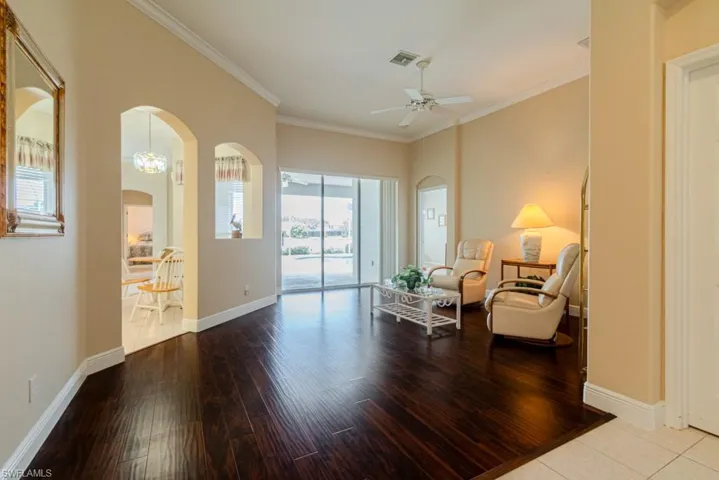 Living area featuring tile floors, ceiling fan with notable chandelier, and crown molding