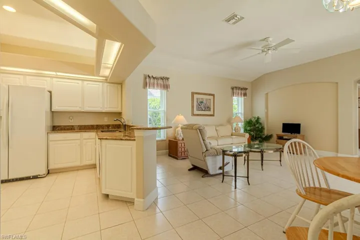 Kitchen with white refrigerator, light tile flooring, ceiling fan, white cabinetry, and dark stone countertops