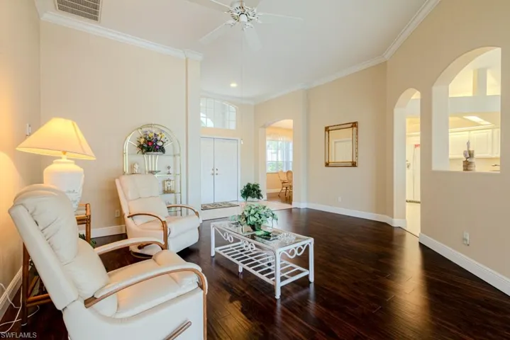 Living room with ceiling fan, ornamental molding, and dark wood-type flooring