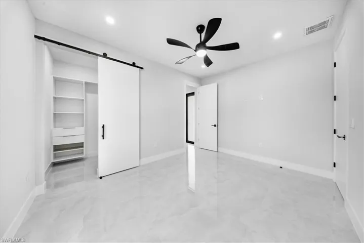 Unfurnished bedroom featuring a barn door, a spacious closet, a ceiling fan, light marble finish flooring, and recessed lighting