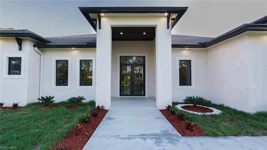 Doorway to property with a yard, roof with shingles, and stucco siding