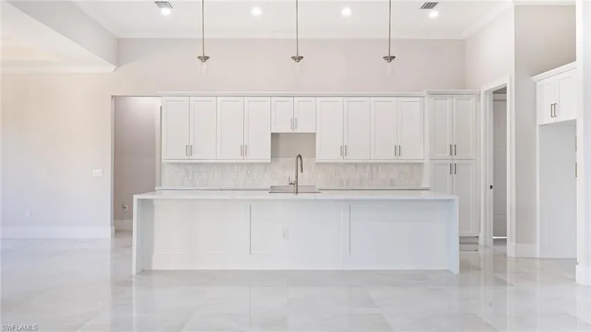 Kitchen featuring tasteful backsplash, a kitchen island with sink, white cabinetry, and a sink