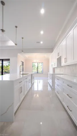 Kitchen with decorative backsplash, ornamental molding, a tray ceiling, white cabinetry, and a sink
