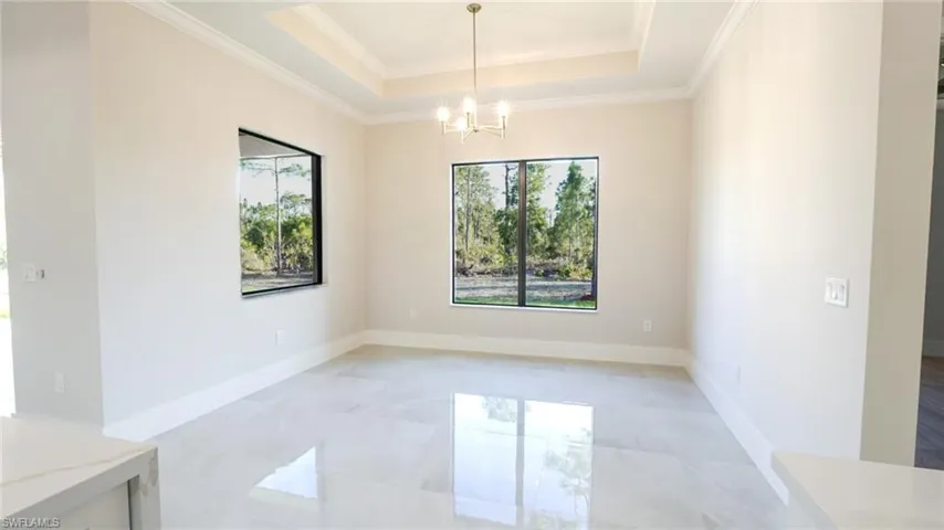Unfurnished room featuring baseboards, a notable chandelier, a raised ceiling, and crown molding