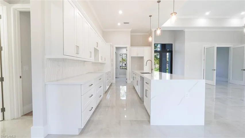 Kitchen with white cabinets, decorative backsplash, ornamental molding, marble finish floor, and a sink