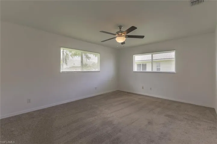 Empty room with carpet floors, ceiling fan, and a healthy amount of sunlight