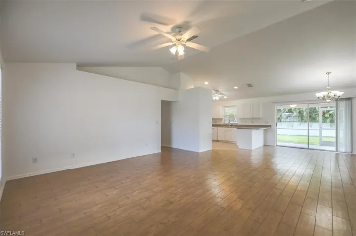 Unfurnished living room featuring vaulted ceiling, light hardwood / wood-style flooring, and ceiling fan with notable chandelier