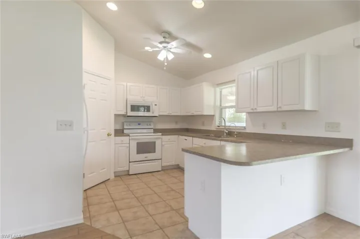 Kitchen with lofted ceiling, white cabinets, kitchen peninsula, white appliances, and ceiling fan