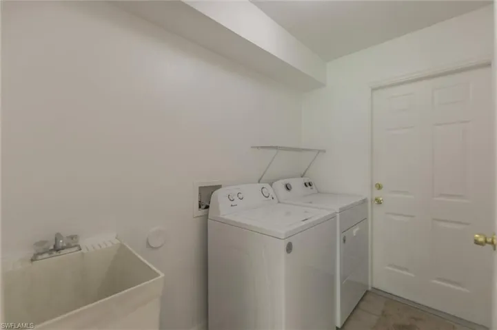 Clothes washing area with sink, light tile patterned flooring, and separate washer and dryer