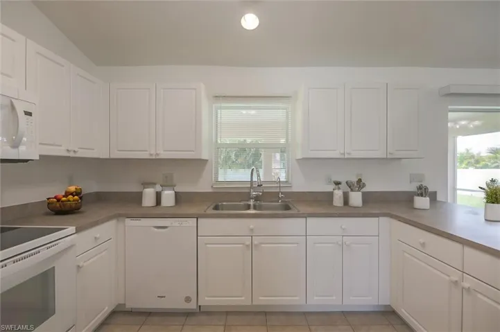 Kitchen with sink, white cabinets, white appliances, and a wealth of natural light