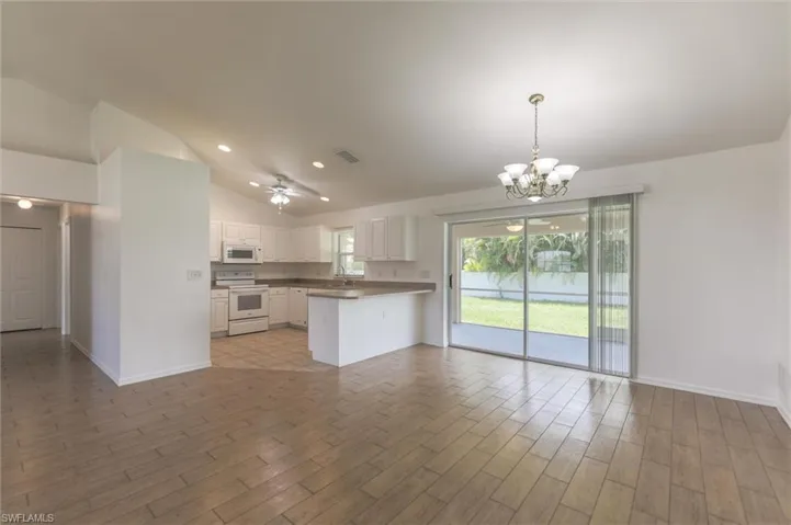 Unfurnished living room with sink, vaulted ceiling, ceiling fan with notable chandelier, and dark wood-type flooring
