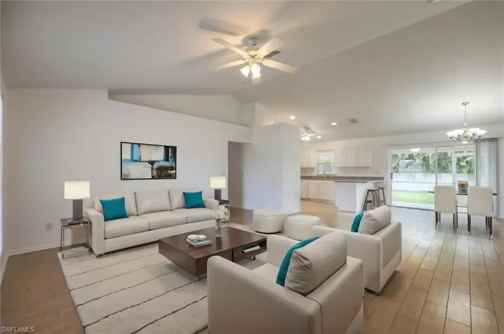 Living room featuring light wood-type flooring, ceiling fan with notable chandelier, and lofted ceiling