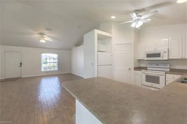 Kitchen with hardwood / wood-style floors, lofted ceiling, white cabinets, white appliances, and ceiling fan