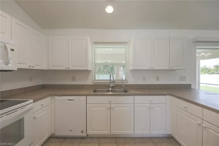 Kitchen with white cabinetry, sink, lofted ceiling, light tile patterned floors, and white appliances
