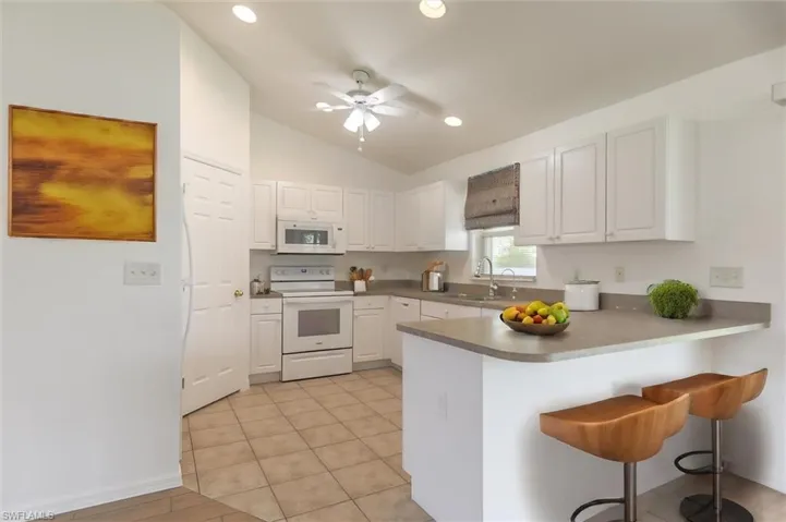 Kitchen with ceiling fan, white cabinets, vaulted ceiling, a breakfast bar area, and white appliances