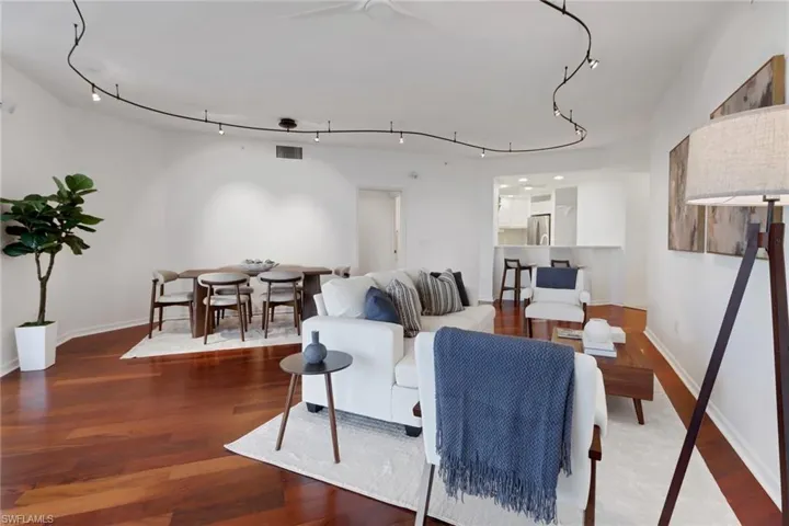 Living room and dining area featuring hardwood flooring and rail lighting. Currently, there is a TV in living area and artwork is in dining area.
