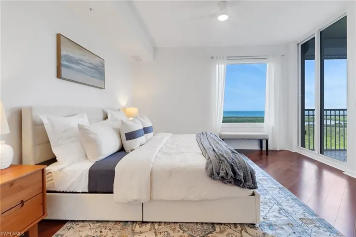 Bedroom with new ceiling fan, king-size bed, dark hardwood floors, access to exterior lanai with views of the gulf, and a wall of windows