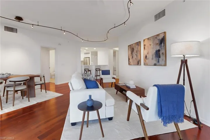 Living and dining areas with hardwood flooring. Currently, paintings are over dining area and there is now a TV in living area.