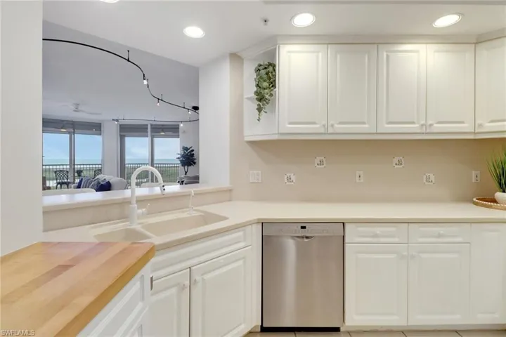 Kitchen with breakfast bar, additional storage with butcher block counter, corian countertops, sink, stainless steel dishwasher, and white cabinets
