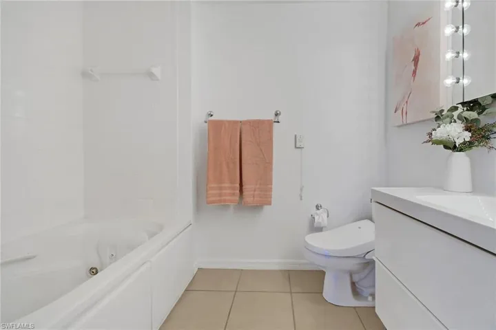 Bathroom with tile patterned floors, toilet, vanity, and a jetted bath